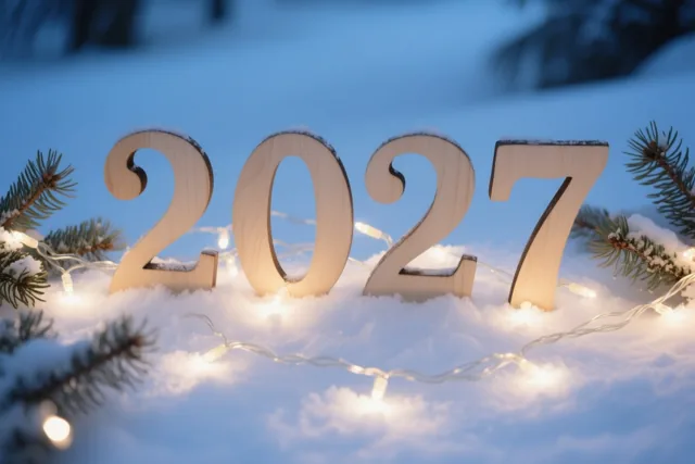 Houten cijfers vormen 2027 in verse sneeuw tussen dennentakken en brandende lichtjes onder een blauwe schemerhemel.