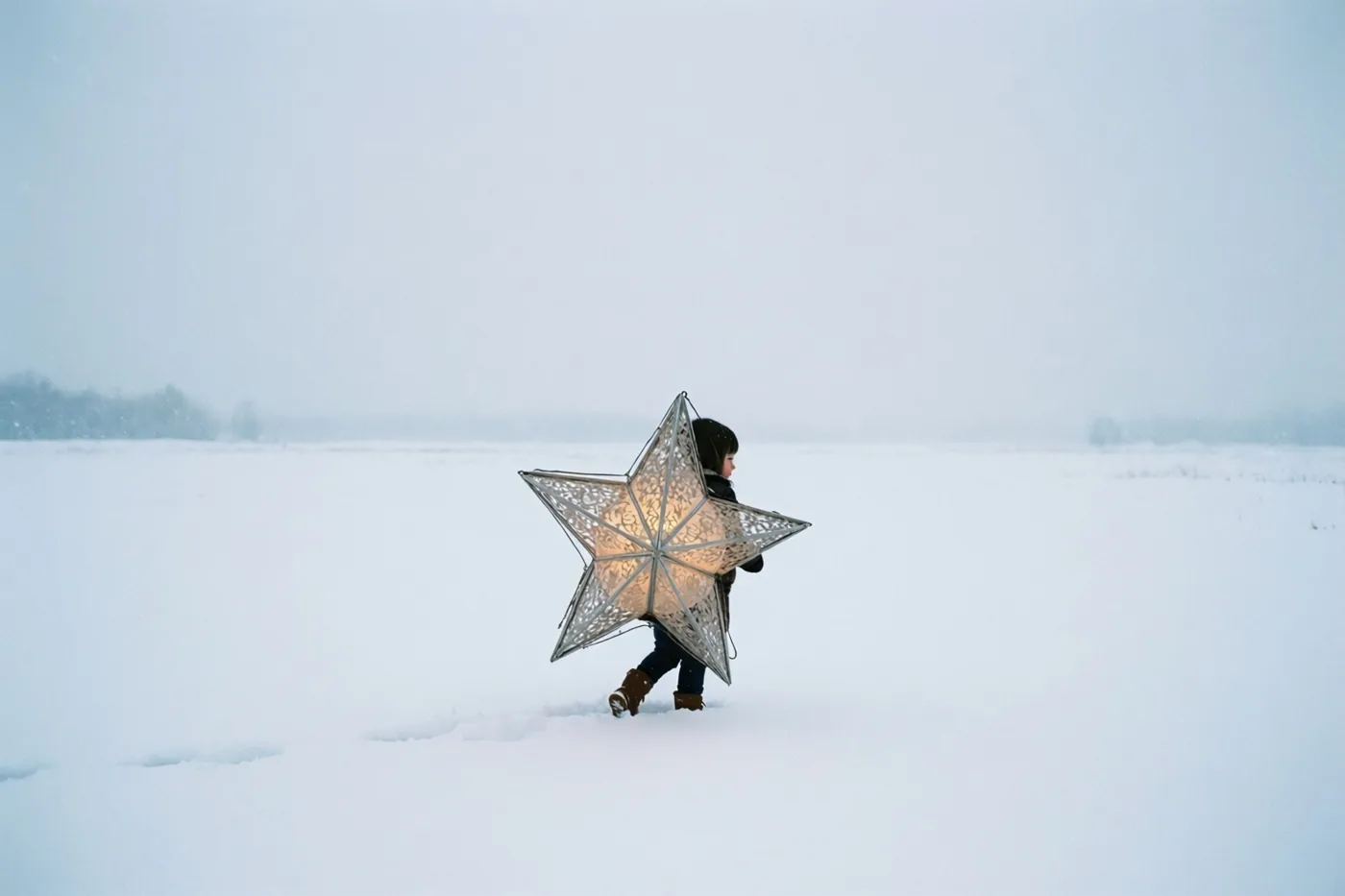 Een klein kind loopt met de rug naar de camera door een uitgestrekt sneeuwveld onder een bewolkte hemel en draagt een verlichte sterlantaarn die groter is dan het kind.