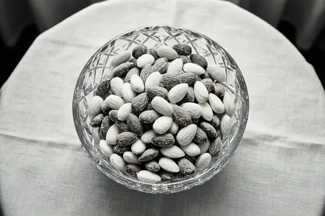Een zwart-witfoto toont een kristallen schaal met witte en zilveren suikerbonen op een tafel met een linnen tafelkleed.