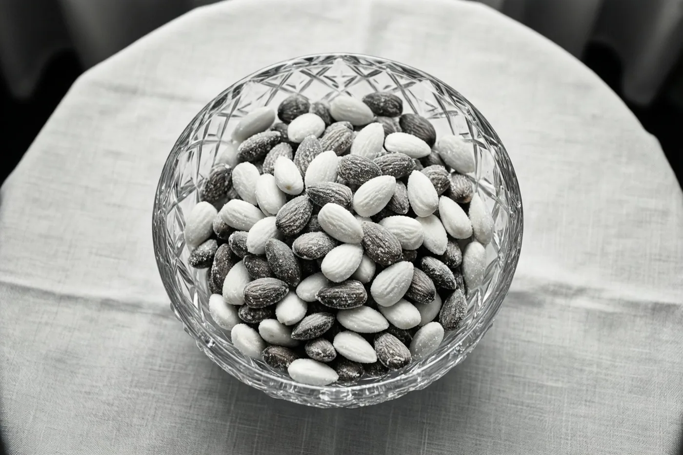 Een zwart-witfoto toont een kristallen schaal met witte en zilveren suikerbonen op een tafel met een linnen tafelkleed.