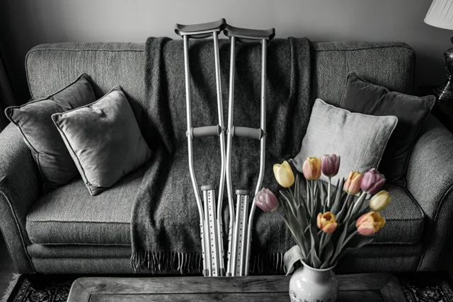 Krukken leunen tegen een grijze zetel met een deken en kussens, terwijl kleurrijke tulpen op een houten tafel afsteken tegen de zwart-witte achtergrond.
