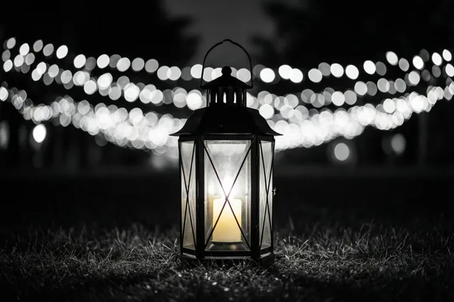 Een brandende lantaarn staat 's nachts op het gras met onscherpe feestlichtjes op de achtergrond, weergegeven in één kleurenpalet.