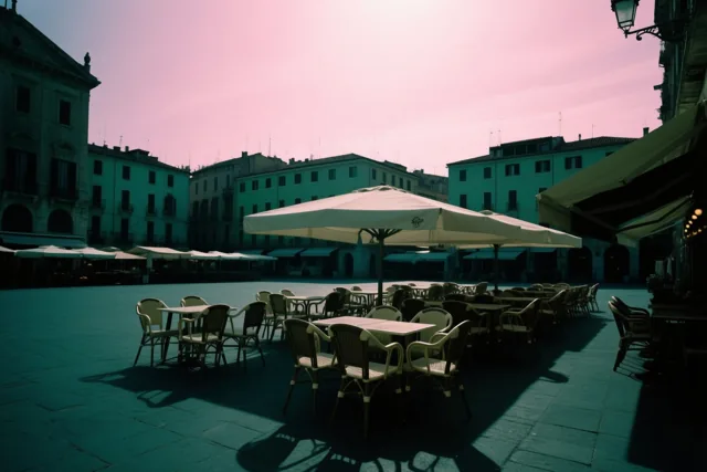 Een leeg caféterras met pas buitengezette stoelen staat op een marktplein onder een roze lucht, in overwegend blauwgroene en roze tinten.