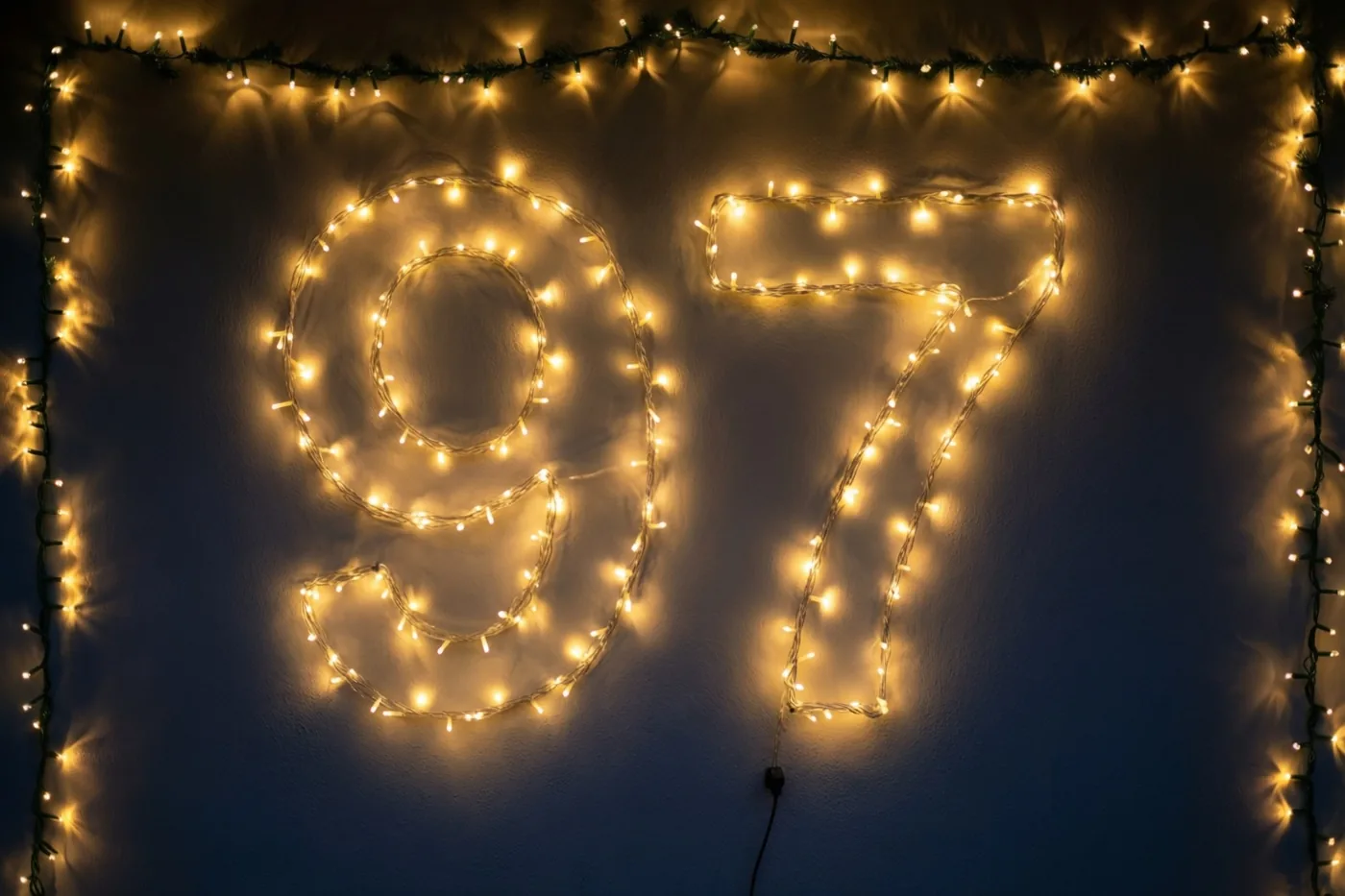 Warme lichtslingers vormen 97 op een donkere muur, met nog meer lichtjes als rand eromheen.
