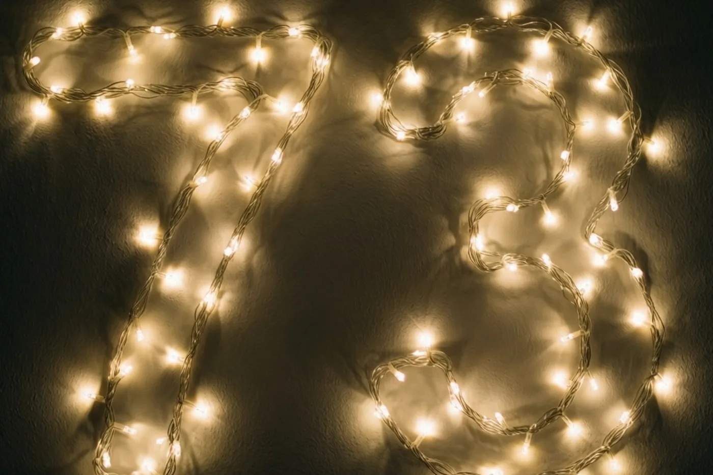 Warme lichtjes vormen het getal 73 tegen een donkere muur met een zachte gouden gloed.