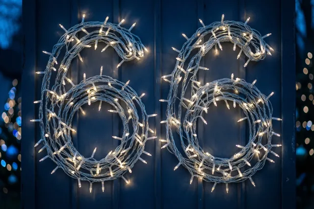 Warme lichtslingers vormen het getal 66 op een donkerblauwe houten muur, met onscherpe lichtjes op de achtergrond.