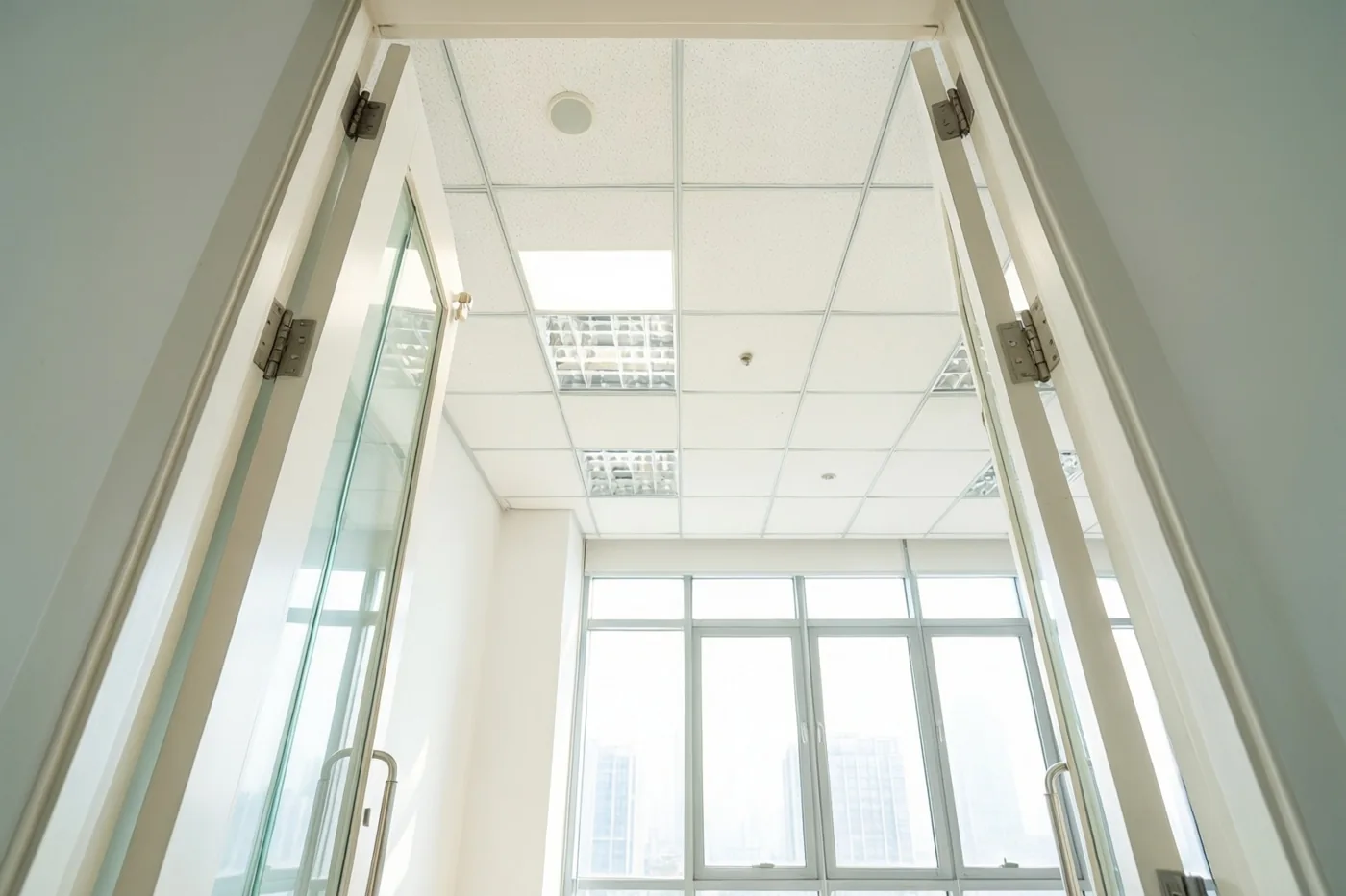 Een open deuropening geeft zicht op een lege, lichte kantoorruimte met een hoog plafond en grote ramen in witte en lichtgrijze tinten.