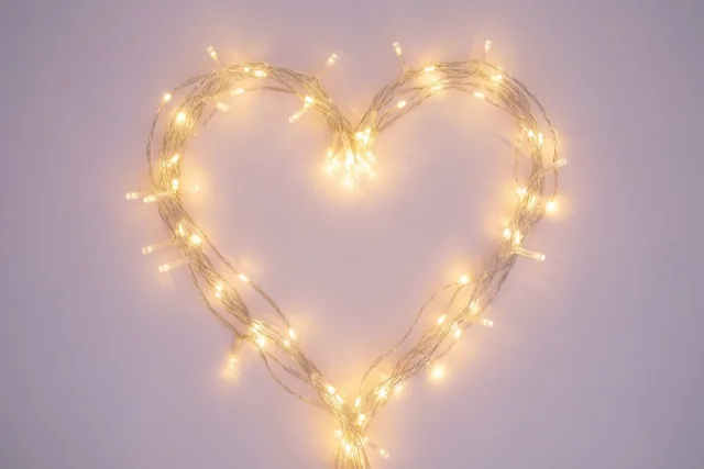 Gloeiende lichtjes vormen een hart tegen een zachte lavendelkleurige achtergrond, in gele en lichtpaarse tinten.