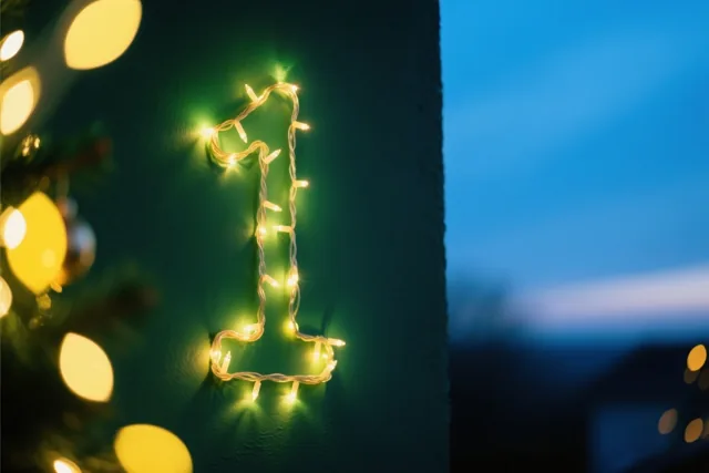 Warme lichtjes vormen het cijfer 1 op een donkergroene muur, met een wazige blauwe achtergrond en feestelijke lichtjes.