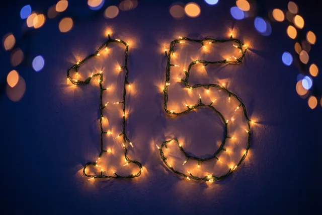 Het getal 15 is gevormd door warme lichtjes op een donkerblauwe muur, met wazige feestlichtjes op de achtergrond.