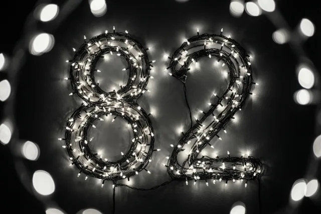 Lichtjes vormen het getal 82 op een donkere muur, omringd door onscherpe lichtvlekken in dezelfde kleurtint.