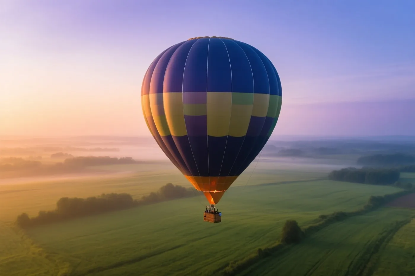 Een kleurrijke luchtballon zweeft bij zonsopgang boven een uitgestrekt groen veld met mist in de dalen, onder een oranje, paarse en blauwe lucht.