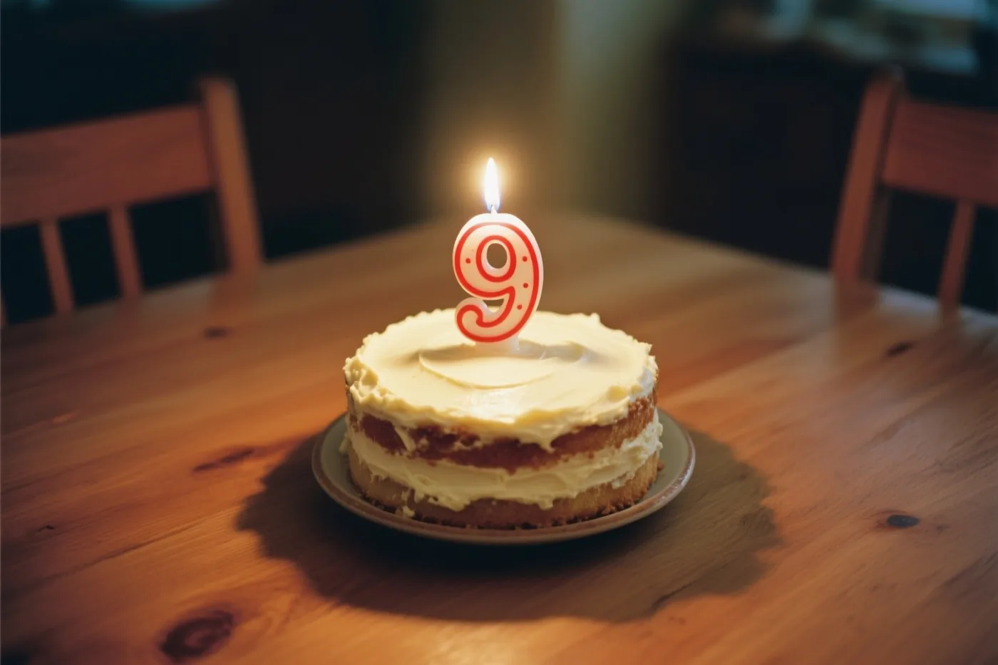 Een kleine huisgemaakte roomtaart met één brandend kaarsje in de vorm van een 9 staat op een houten tafel in warm kaarslicht.