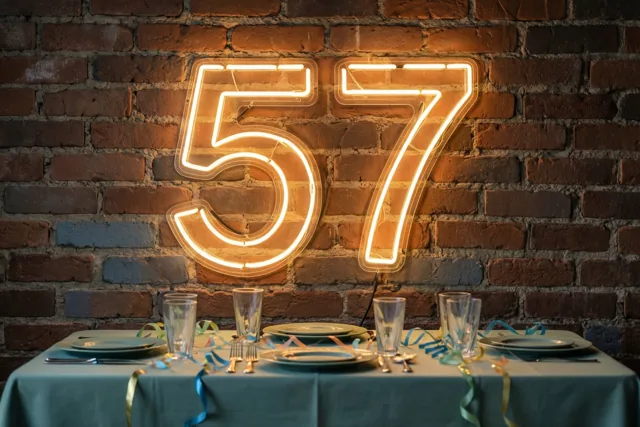 Een warm gloeiend neonbord met 57 hangt aan een bakstenen muur boven een tafel met borden, glazen, slingers en een blauwgroen tafelkleed.