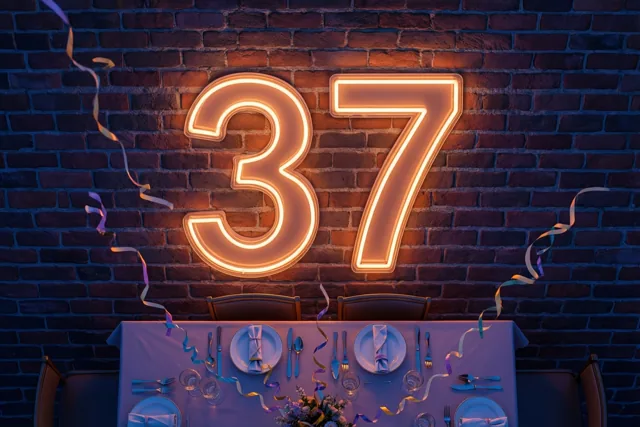 Een warm verlicht neonbord met 37 hangt aan een donkere bakstenen muur boven een gedekte feesttafel met een paars tafelkleed en kleurrijke slingers.