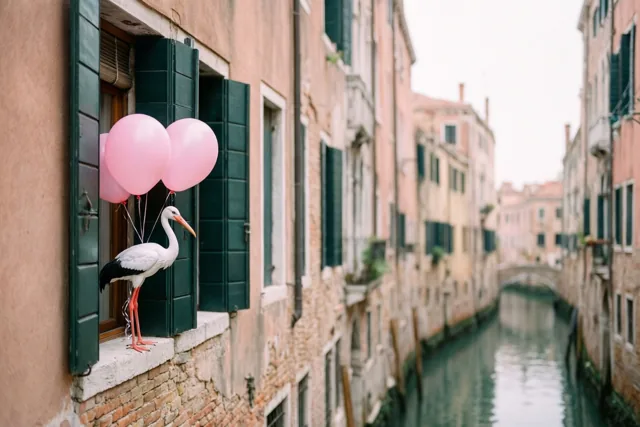 Een ooievaarsbeeldje met roze ballonnen zit op de vensterbank van een oud gebouw aan een smalle gracht, met gevels in warme tinten op de achtergrond.