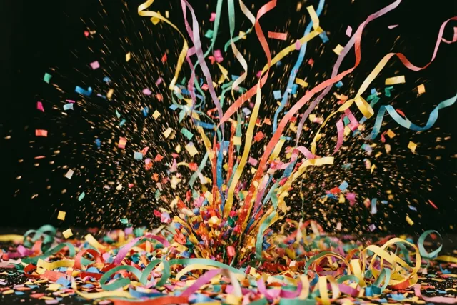 Rode, gele, blauwe en groene slingers en confetti schieten omhoog uit een hoop tegen een donkere achtergrond.