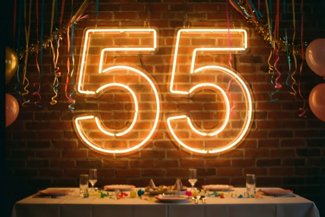 Een oranje neongetal 55 hangt aan een rode bakstenen muur boven een feesttafel, tussen kleurrijke slingers en ballonnen.