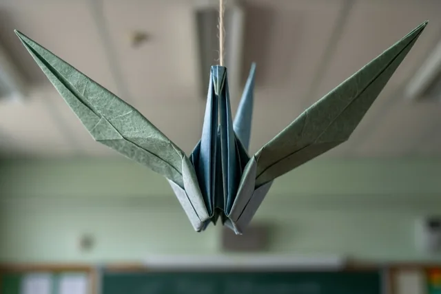 Een mobiel met gevouwen papieren vogels in gedempte groene en blauwe tinten hangt aan een klasplafond, van onderen gezien.