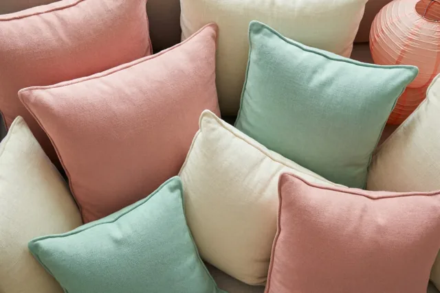 Pastelkleurige kussens in roze, mintgroen en crème liggen op een zetel, met een papieren lantaarn op de achtergrond.