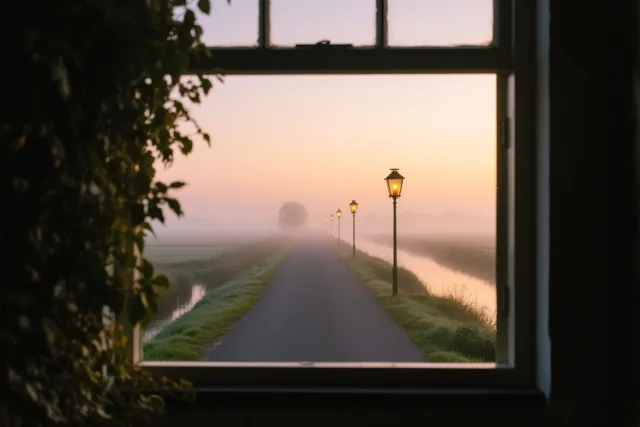 Door een raam is een polderweg bij schemering te zien, met brandende lantaarns die verdwijnen in de mist onder een oranje en paarse lucht.