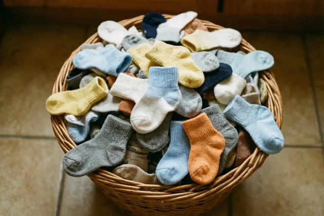 Een rieten wasmand vol kleine babysokjes in pastelkleuren en neutrale tinten staat op een tegelvloer in zacht licht.