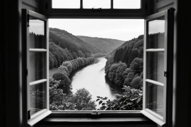 Een zwart-witfoto toont door een open raam een kronkelende rivier tussen beboste heuvels.
