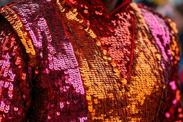 Een carnavalskostuum met overlappende pailletten in rood, roze en oranje is van dichtbij te zien.