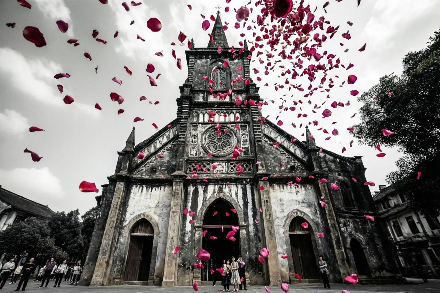 Vanuit een laag standpunt zijn felrode rozenblaadjes te zien die voor een verweerde gotische kerk vallen, onder een bewolkte lucht met mensen in de verte.