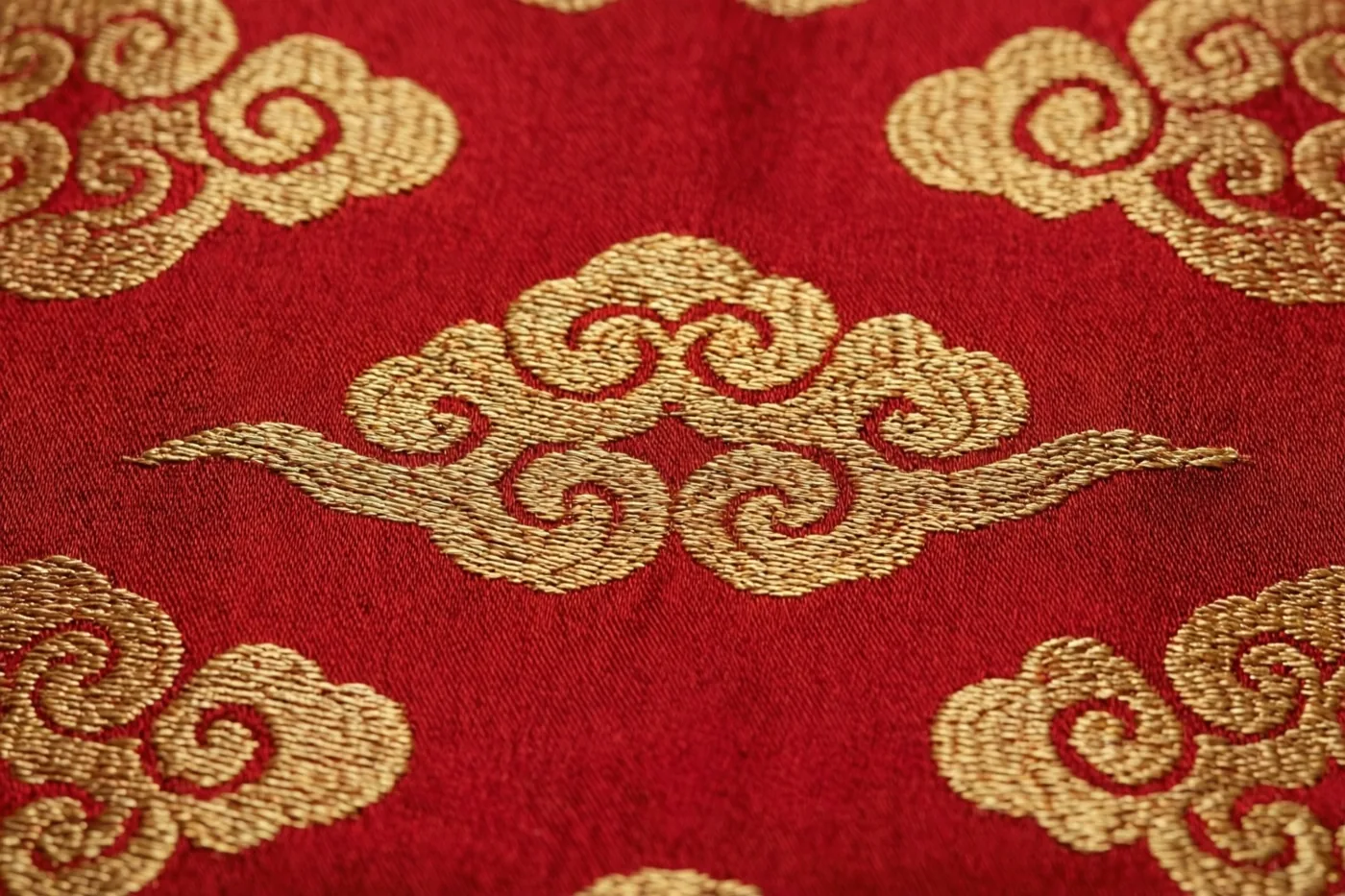 Een detailopname toont dieprode zijde met een fijn ingeweven gouden wolkenpatroon.