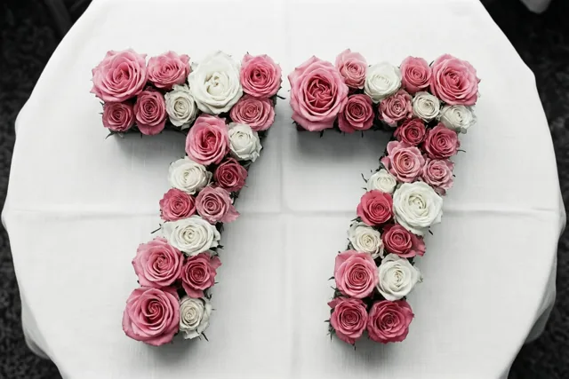 Roze en witte rozen vormen het getal 77 op een wit tafellaken, van bovenaf gezien.