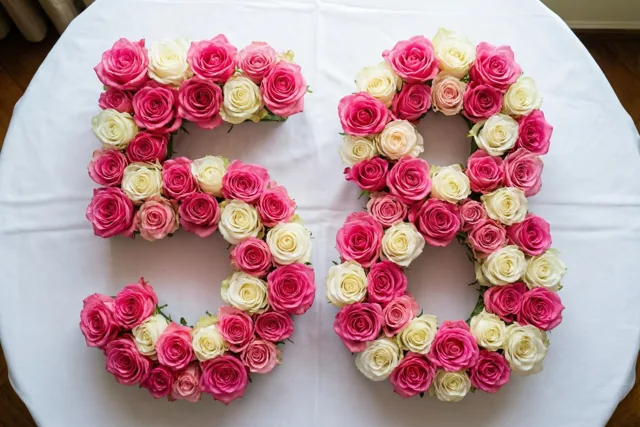 Roze en witte rozen vormen het getal 58 op een wit tafelkleed, van recht bovenaf gefotografeerd.