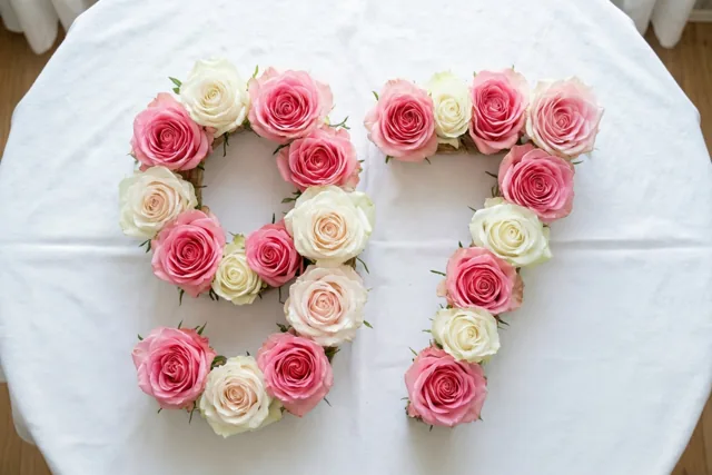 Roze en witte rozen vormen het getal 97 op een wit tafelkleed, van bovenaf gefotografeerd in zachte pasteltinten.