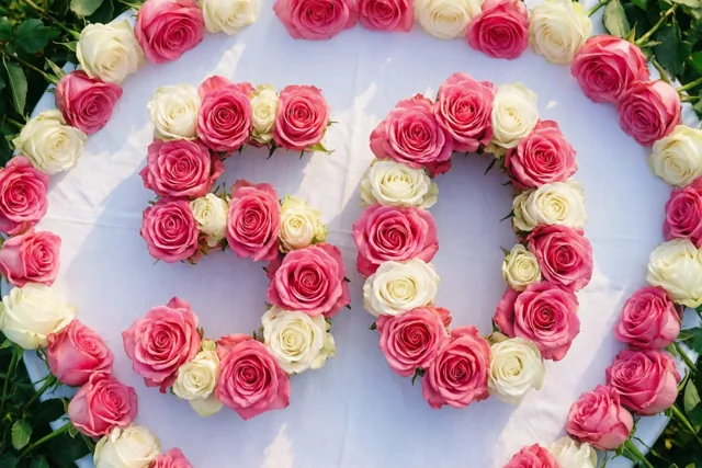 Van bovenaf is 50 te zien, gevormd door roze en witte rozen op een wit tafelkleed in een lichte omgeving.