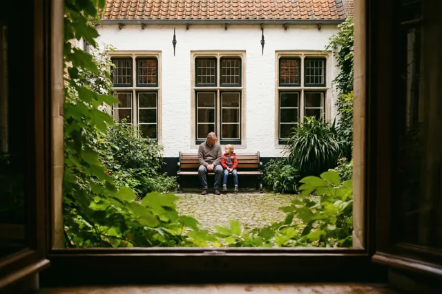 Een vader en kind zitten op een houten bank in een rustige binnenplaats, omringd door groen gebladerte en witte muren in zacht daglicht.