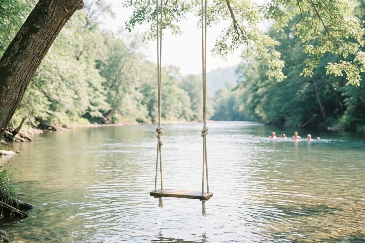 Een houten schommel aan touwen hangt boven een kalme rivier in een weelderig groen bos, met zwemmers in de verte onder fel zonlicht.