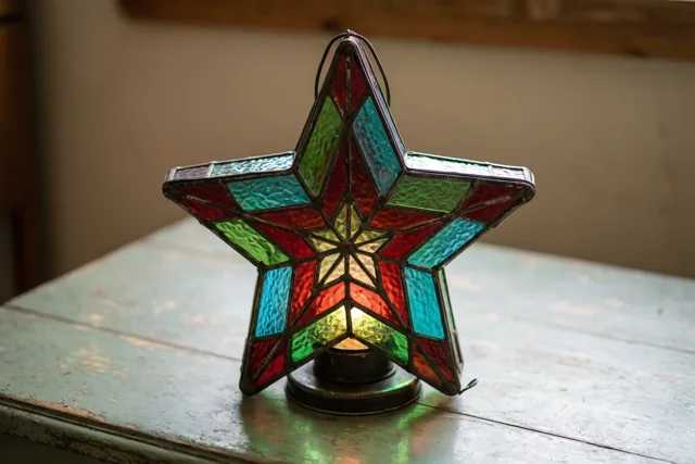 Een brandende sterlantaarn met rode, groene en blauwe glas-in-loodpanelen staat op een verweerde lichtgroene houten tafel en werpt gekleurde weerspiegelingen op het blad.