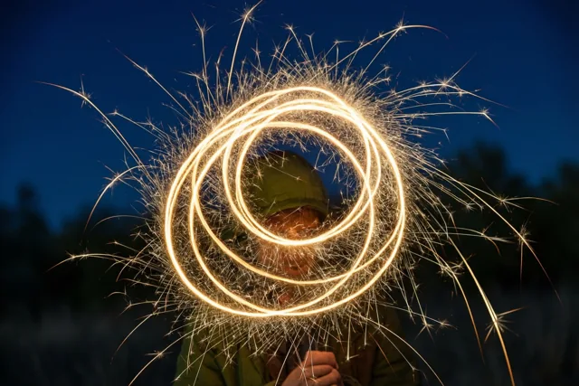 Een persoon met een groene kap houdt een sterretje vast dat goudgele lichtcirkels vormt tegen een diepblauwe nachthemel.