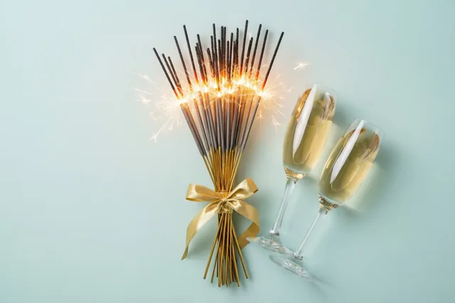 Een bundel niet-brandende sterretjes met een gouden lint staat naast twee champagneglazen tegen een lichtblauwe achtergrond.
