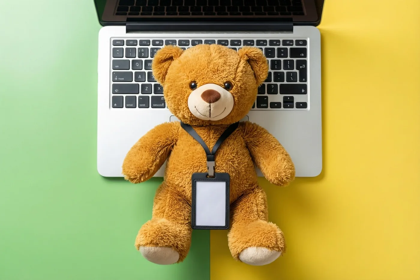 Een bruine teddybeer met een onbedrukt halskoord zit op het toetsenbord van een laptop tegen een achtergrond met een groen en een geel vlak.