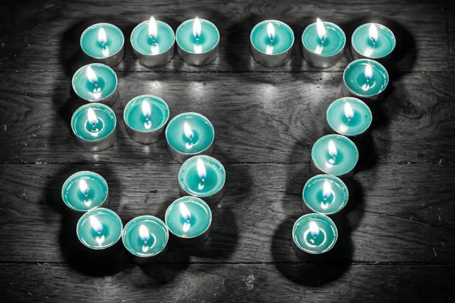 Brandende theelichtjes vormen 57 op een donkere houten vloer in een beeld met blauwgroene en zwarte tinten.