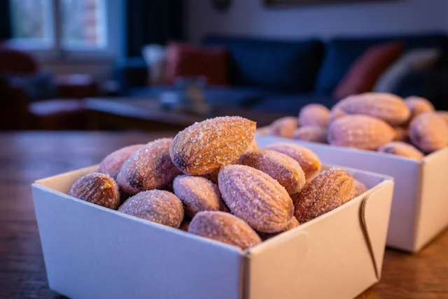 Twee witte kartonnen doosjes met suikerbonen staan op een houten tafel in een warm verlichte woonkamer met zachte pasteltinten en onscherpe meubels op de achtergrond.