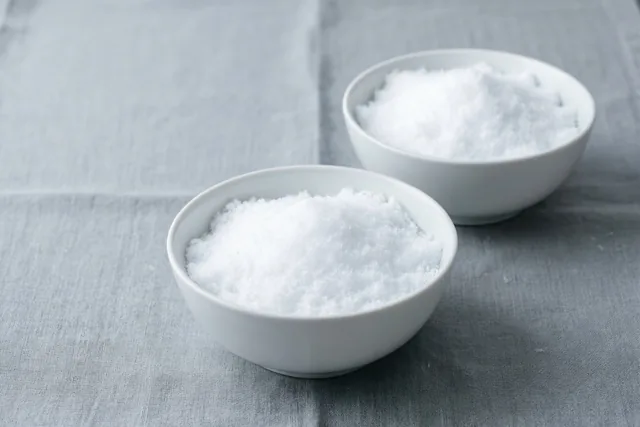 Twee witte porseleinen schaaltjes met verse sneeuw staan op grijs linnen in zacht licht.