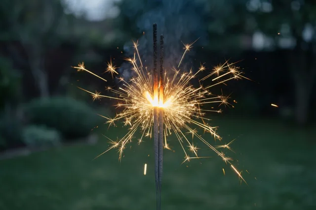Twee sterretjes worden dicht bij elkaar gehouden en verspreiden gouden vonken in een donkere tuin met een wazige groene achtergrond.