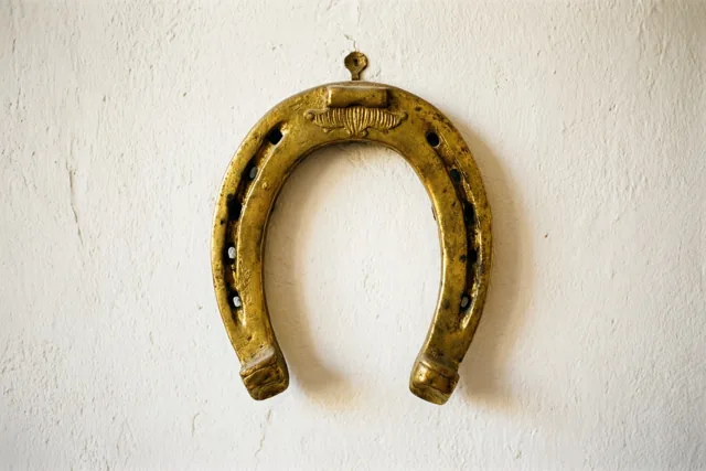 Een verguld hoefijzer hangt aan een witte pleistermuur.