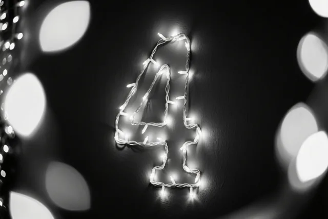 Gloeiende lichtjes vormen het cijfer 4 op een donkere muur, met onscherpe lichtjes op de achtergrond.