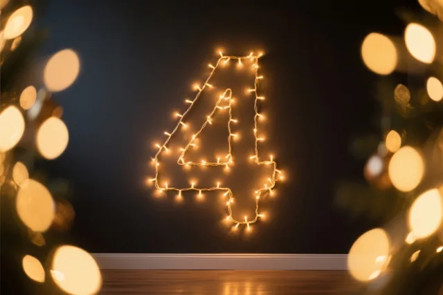 Warme lichtjes vormen het cijfer 4 op een donkere muur boven een houten vloer, met onscherpe lichtvlekken op de voorgrond.