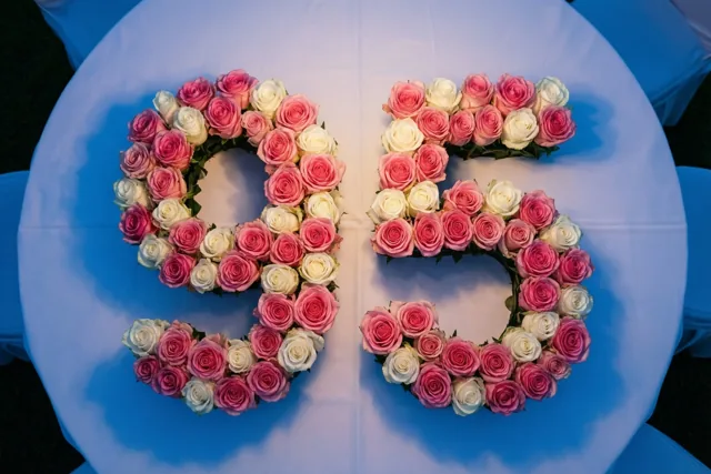 Roze en witte rozen liggen in de vorm van 95 op een wit tafellaken, recht van boven gefotografeerd.