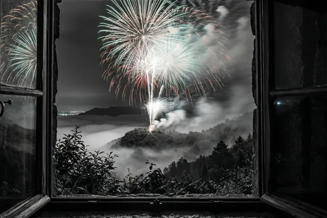 Een open raam met donker hout omlijst een nachtelijke mistige vallei in monochrome tinten, met wit, groen en rood vuurwerk erboven.