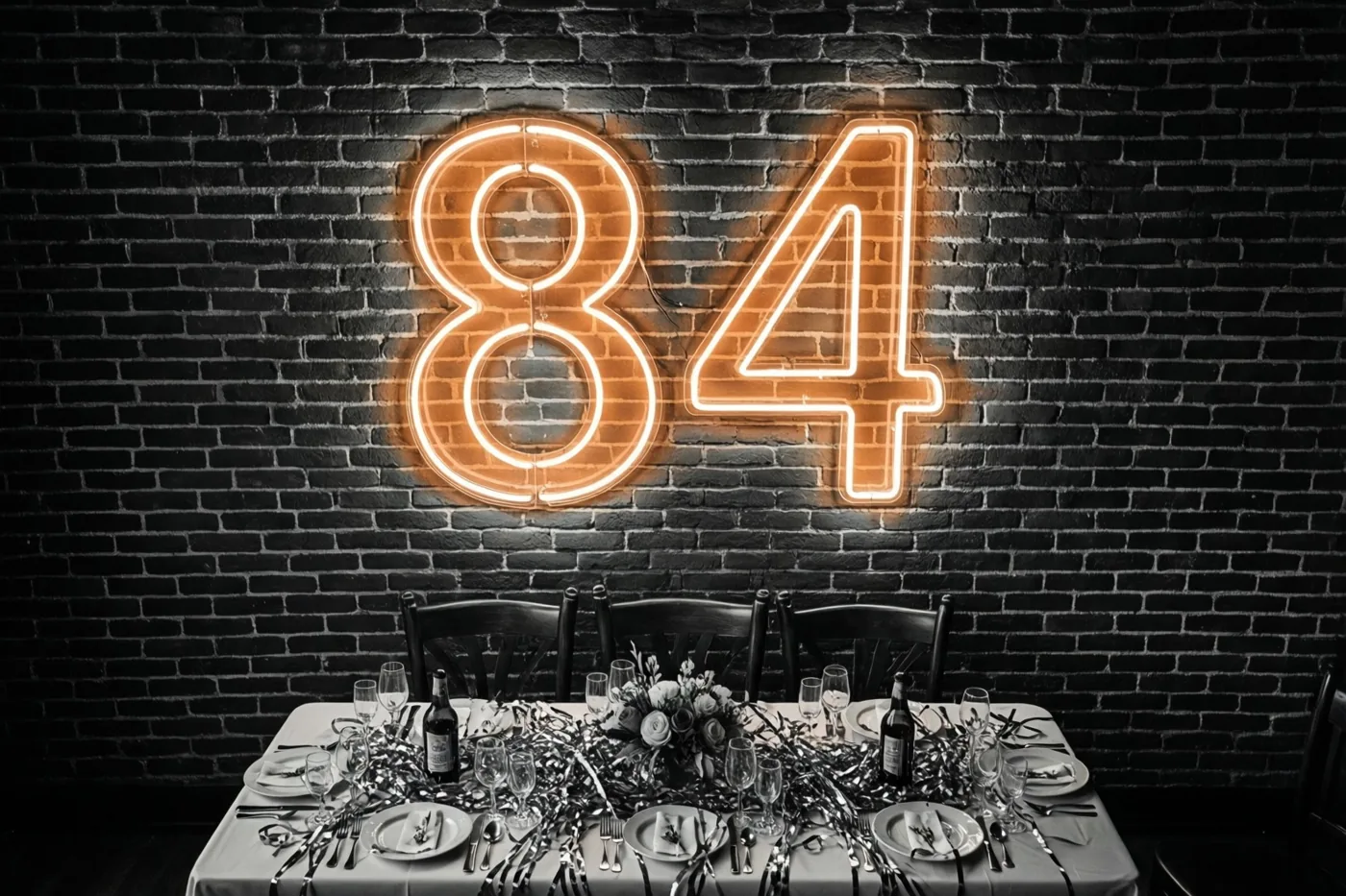 Een warm verlichte neon-84 hangt op een donkere bakstenen muur boven een feestelijk gedekte tafel met slingers en servies.